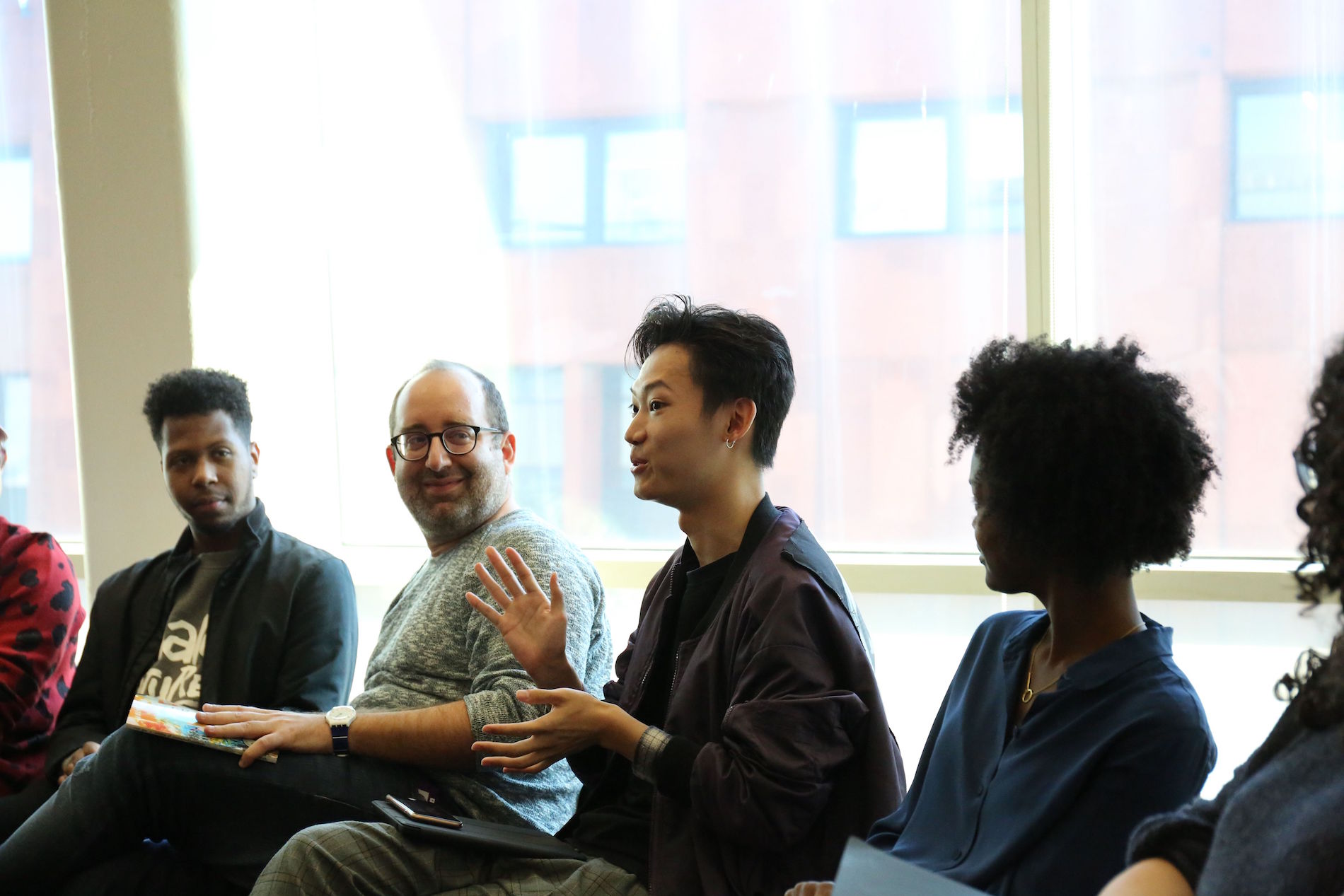 Four students sit in a row, focused on center person talking during Language as Action class